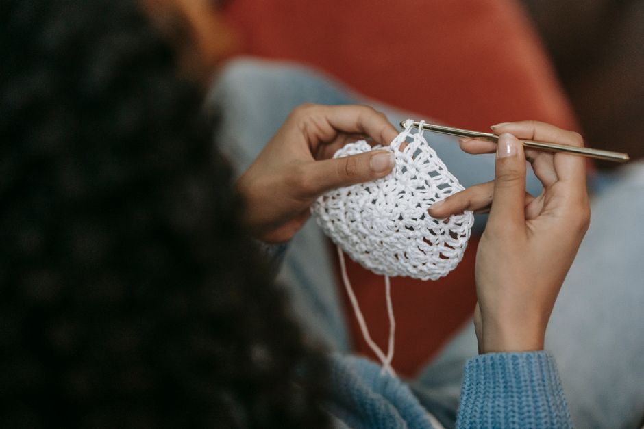 A detailed view of hands crocheting a white piece of fabric with a crochet hook.
