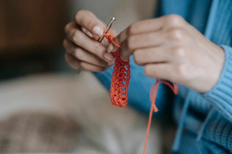 A person skillfully crocheting with vibrant orange yarn in a cozy indoor setting.