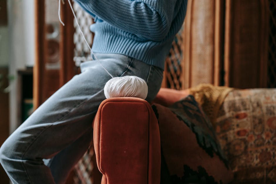 Close-up of an adult knitting indoors, with white yarn and cozy decor.