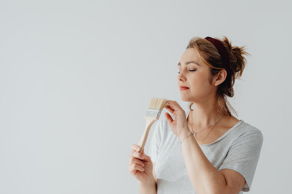 Serene woman artist contemplating with paintbrush in a minimalist indoor setting.