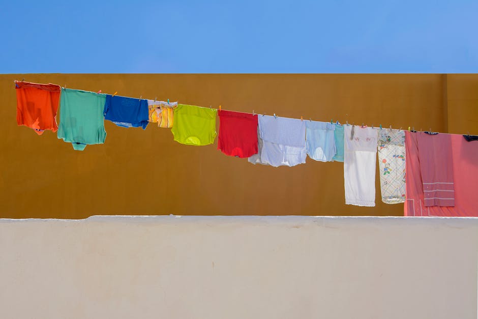 A vibrant clothesline with multicolored laundry against a solid wall under a clear blue sky.
