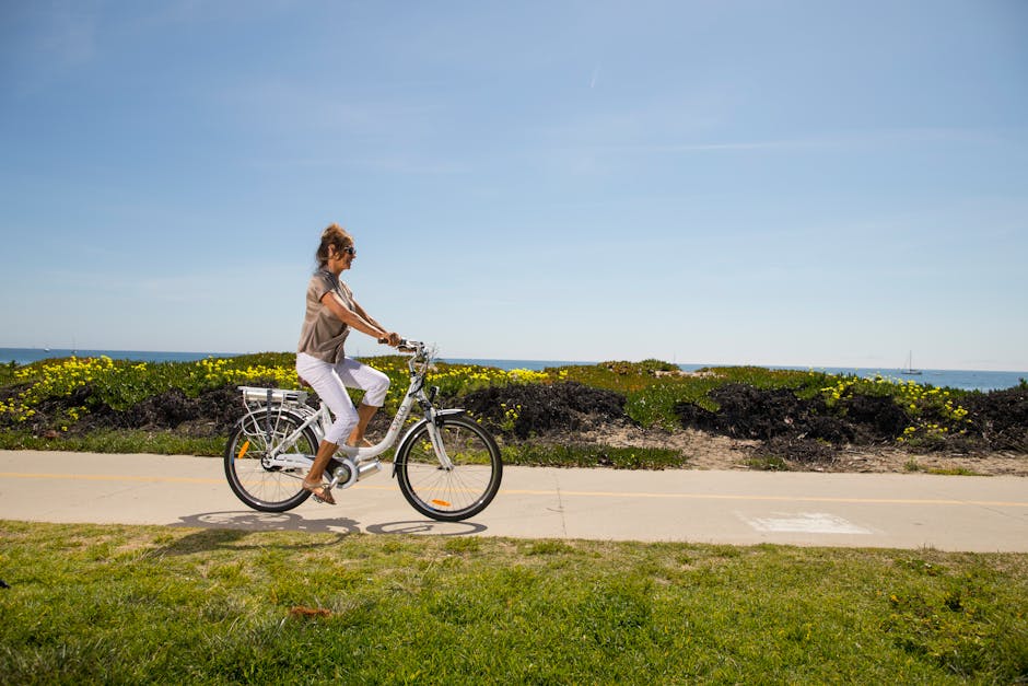 A woman enjoys a ride on an electric bike along a scenic beachside path.