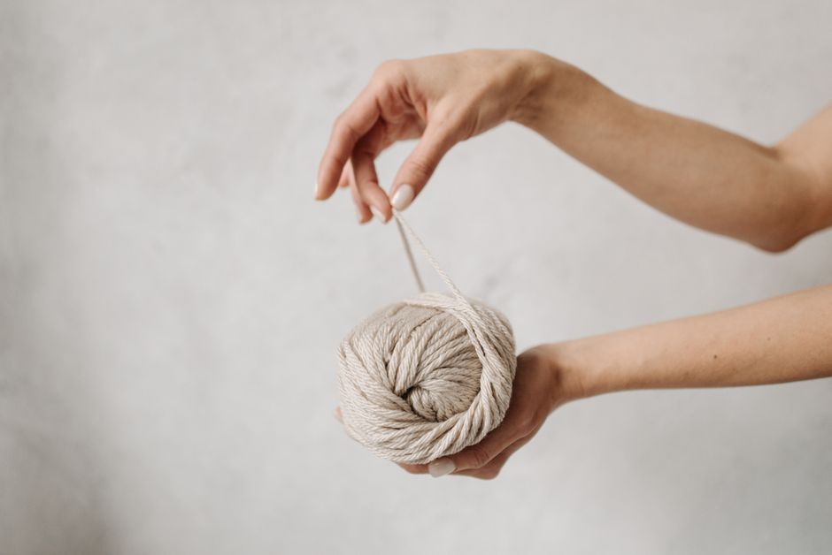 Close-up of a hand holding a beige yarn ball on a neutral background, perfect for crafting