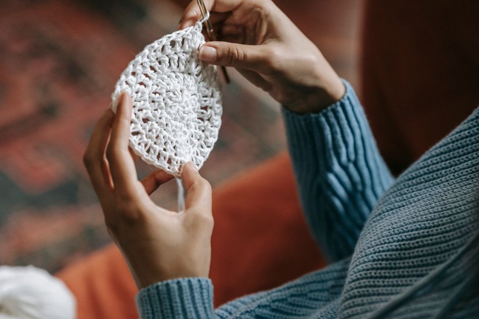 Close-up view of hands knitting a delicate white crochet pattern, highlighting the details
