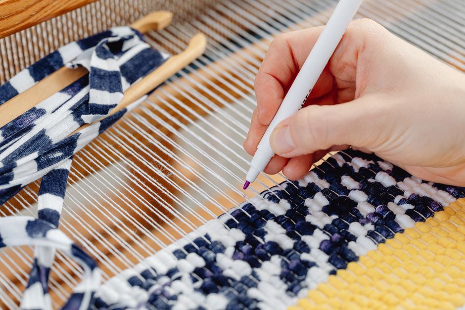 Detailed image showing a hand weaving colorful fabric using a loom.