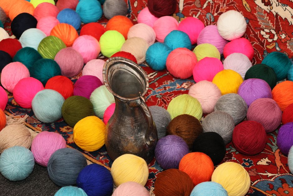 Colorful yarn balls and a metal jug on a traditional patterned rug, creating a vivid, artistic scene.