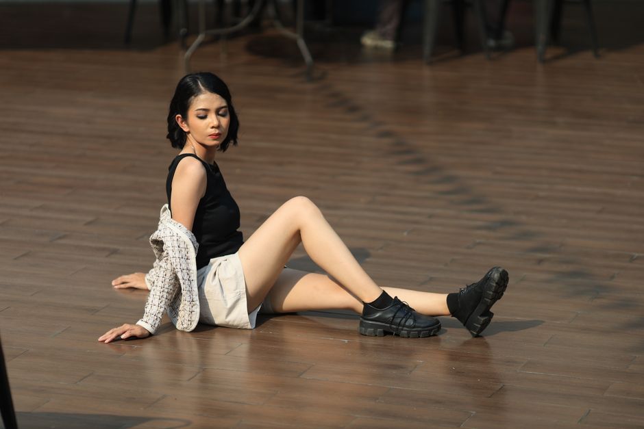 Young woman sitting on a wooden floor in an urban setting, wearing casual summer attire.